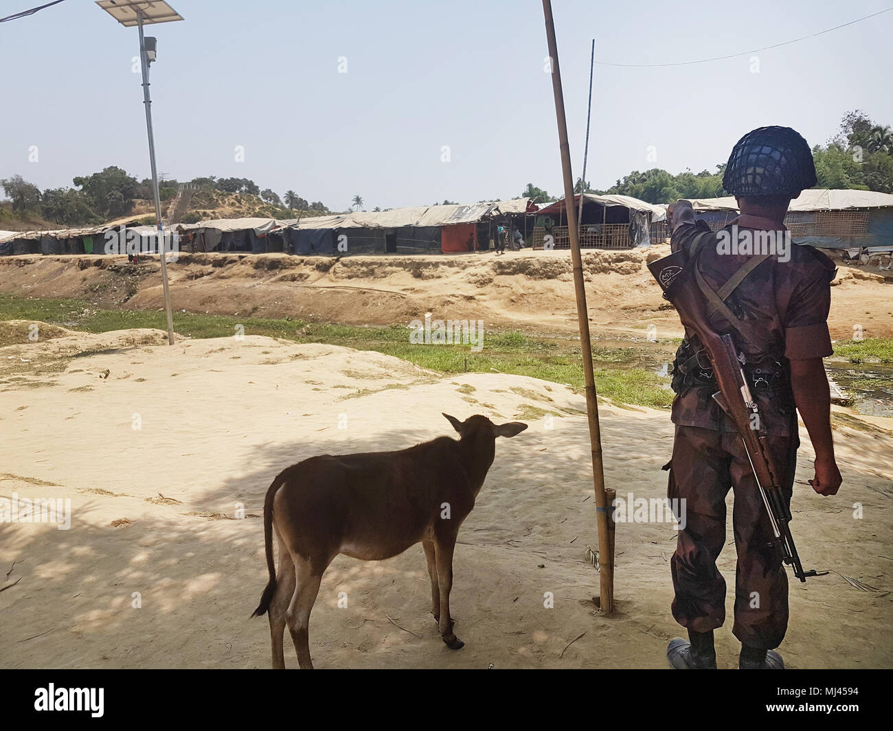13 April 2018, Bangladesh, Cox's Bazar: A Bangladeshi soldier points at a border canal which separates the country from Myanmar. He shows a Rohingya refugee camp in no man's land. A fence, guarded by Burmese soldiers, lies behind the camp. Photo: Nick Kaiser/dpa Stock Photo