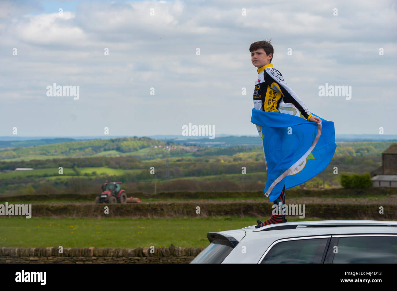 Barnsley, South Yorkshire, UK. 4th May, 2018. A spectator on the roof of a car with his White Rose flag watches the Tour De Yorkshire cyclists reach the top of the hill at Hoylandswaine near Barnsley, South Yorkshire on Stage Two of the yearly cycling competition. Picture: Scott Bairstow/Alamy Live News Stock Photo