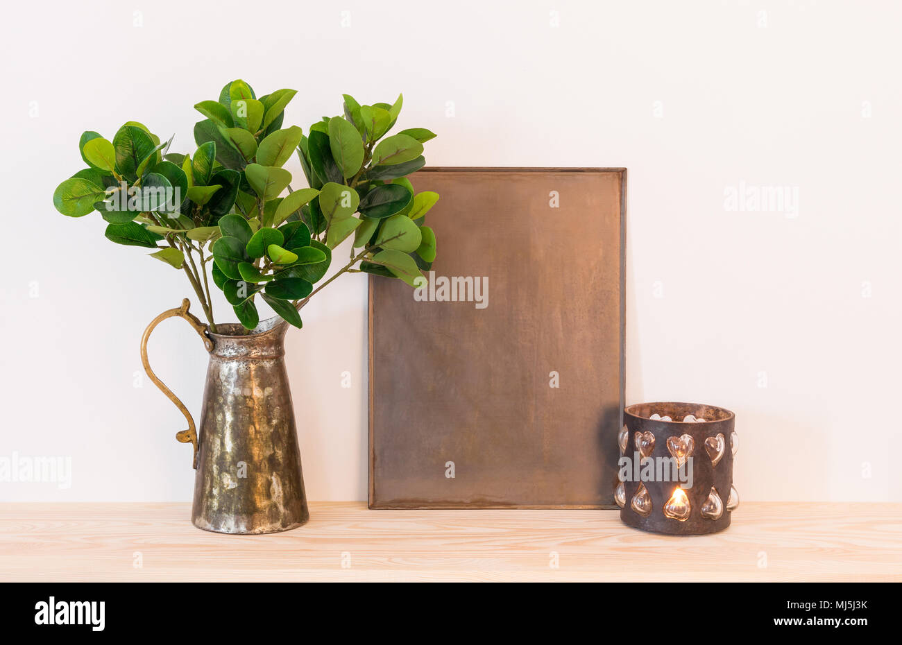 Vintage style home decor composition. Metal frame with copy space, ficus in antique jar and candle. Stock Photo