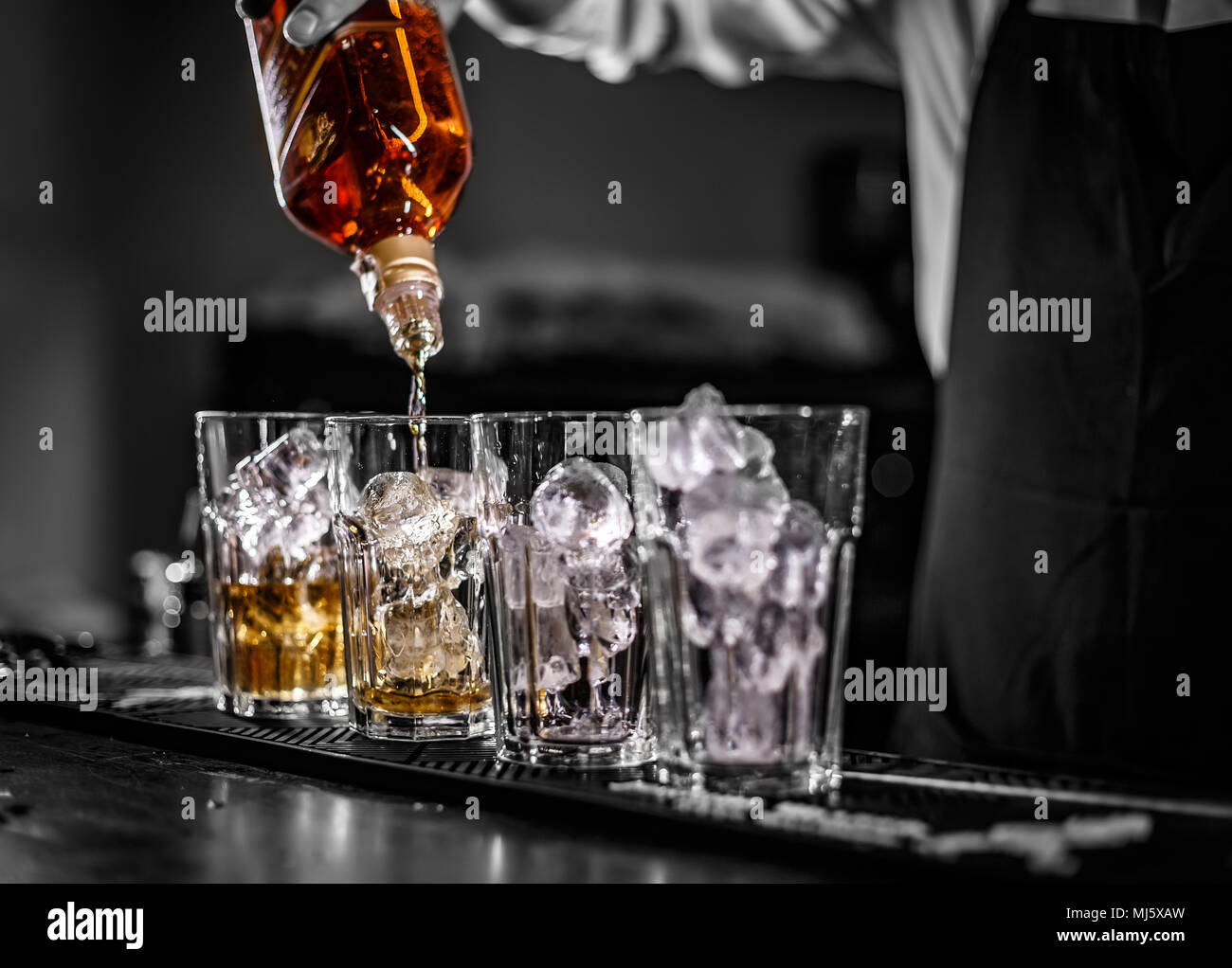 Barman pouring alcoholic drink into the glasses with ice cubes on the bar counter Stock Photo