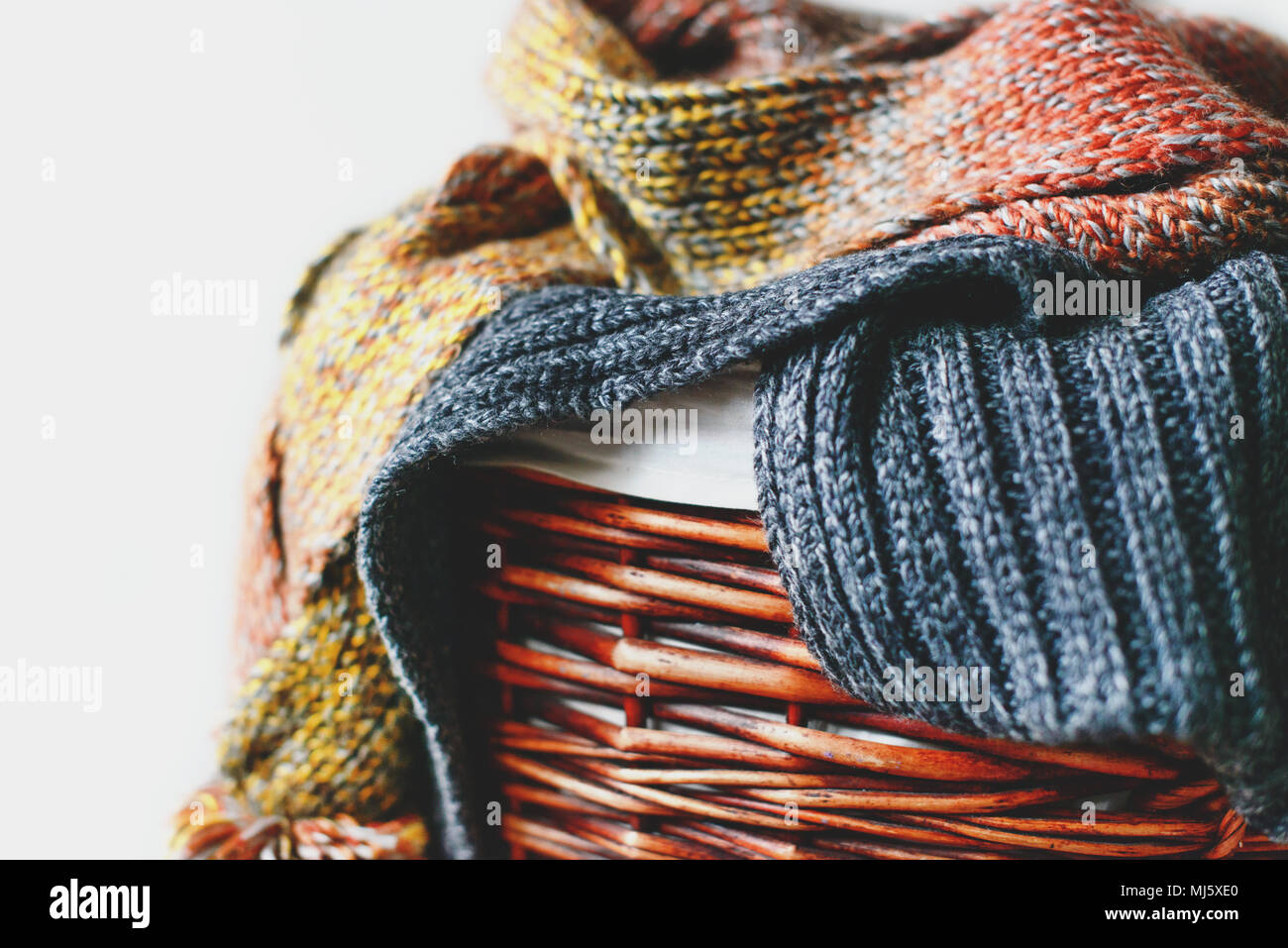 Stack of knitted winter scarfs on straw basket isolated on white background. Stock Photo
