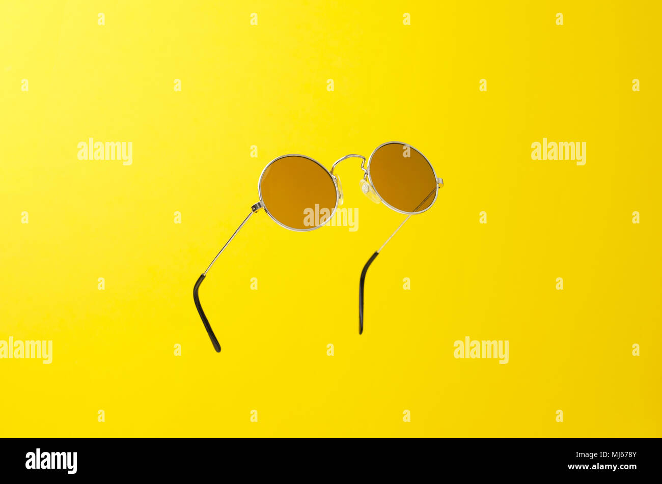 Round Sunglasses in the air over yellow background Stock Photo