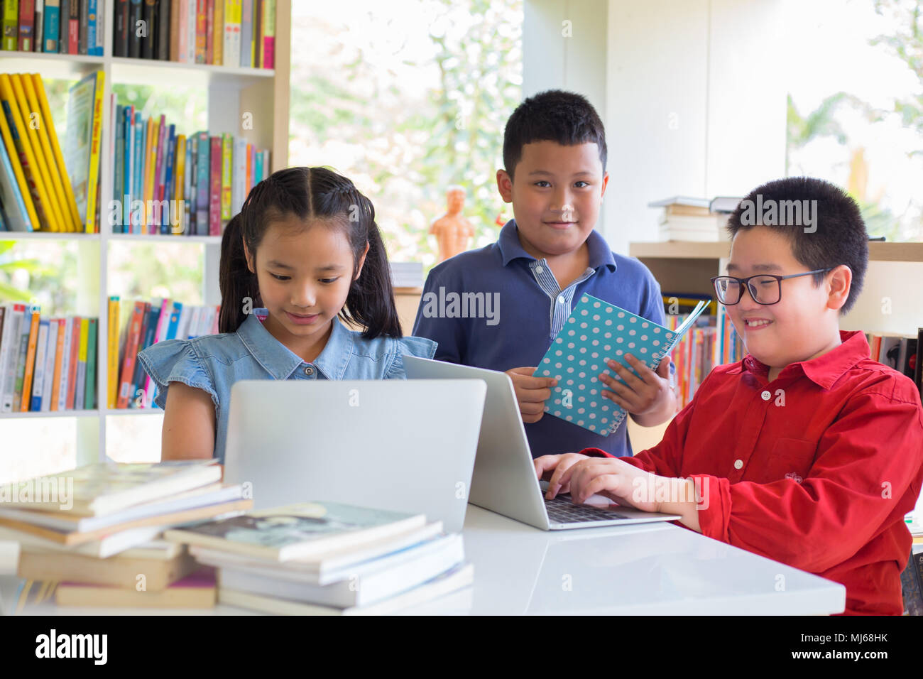 Attentive schoolkid is doing his homework in libary at school. Attentive students  something in their laptop  while sitting at desks in the libry. Bac Stock Photo