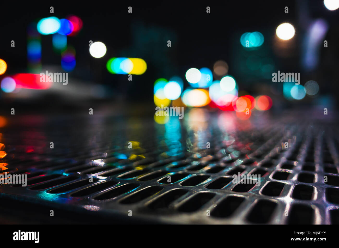 Abstract night city street background, wet sewage grid with colorful blurred lights, natural bokeh effect Stock Photo