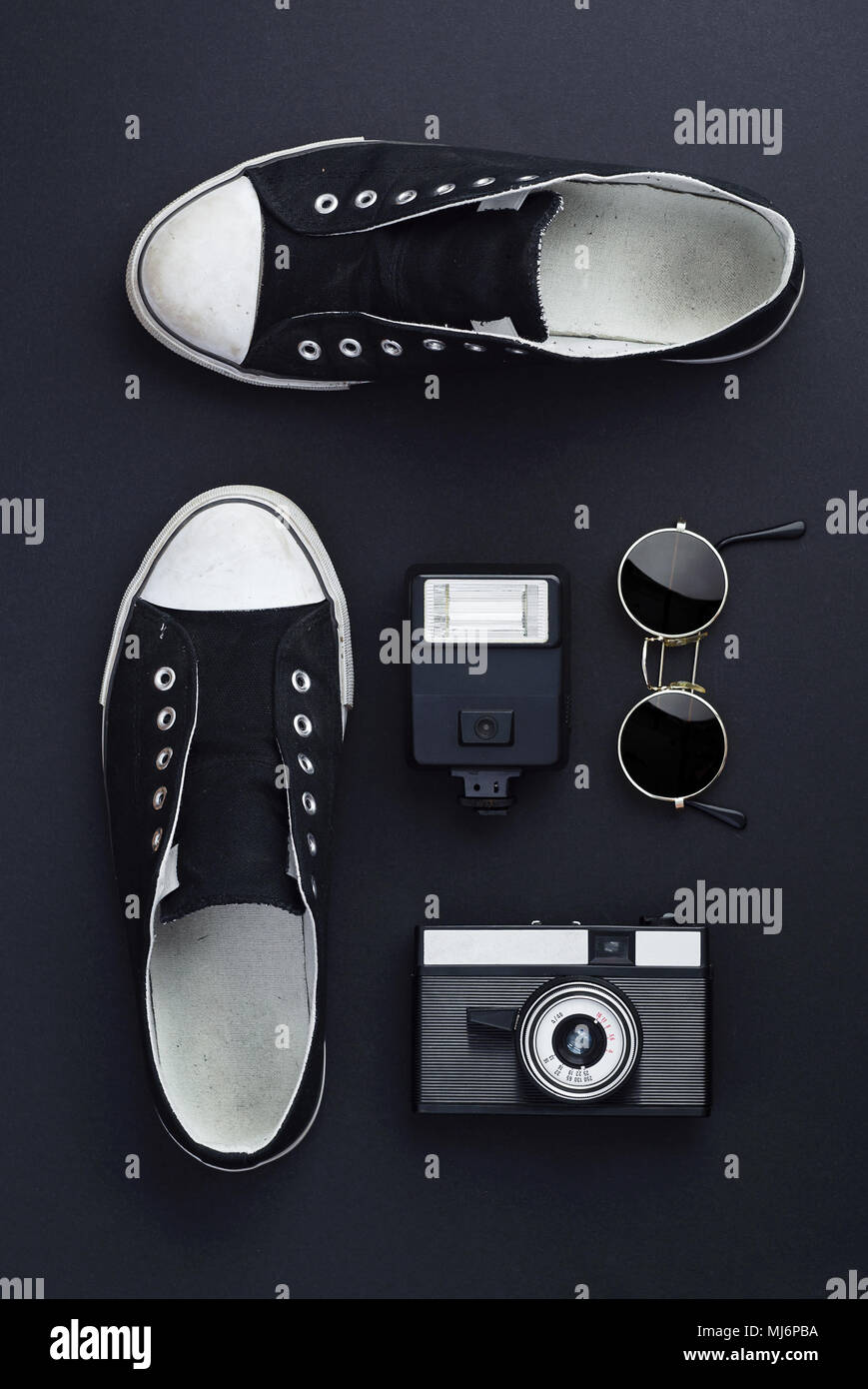 Concept: Ready for a trip. Sneakers, photo camera, and round sunglasses well organized over black background. All the objects are black Stock Photo