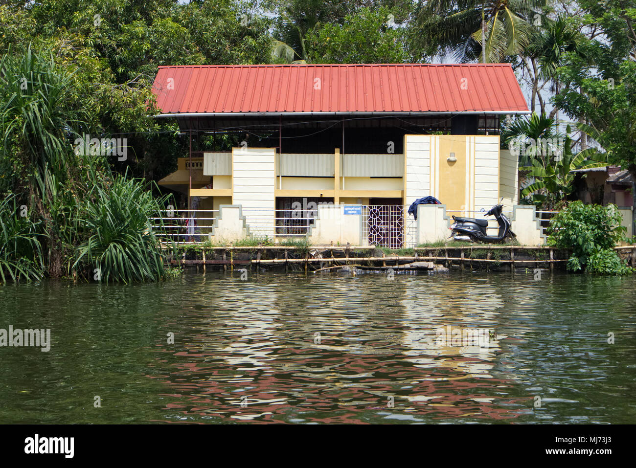 Alappuzha, Kerala / India - April 15 2018: A modern Indian house on the banks of the waterways of Alappuzha reflected in the water. Stock Photo
