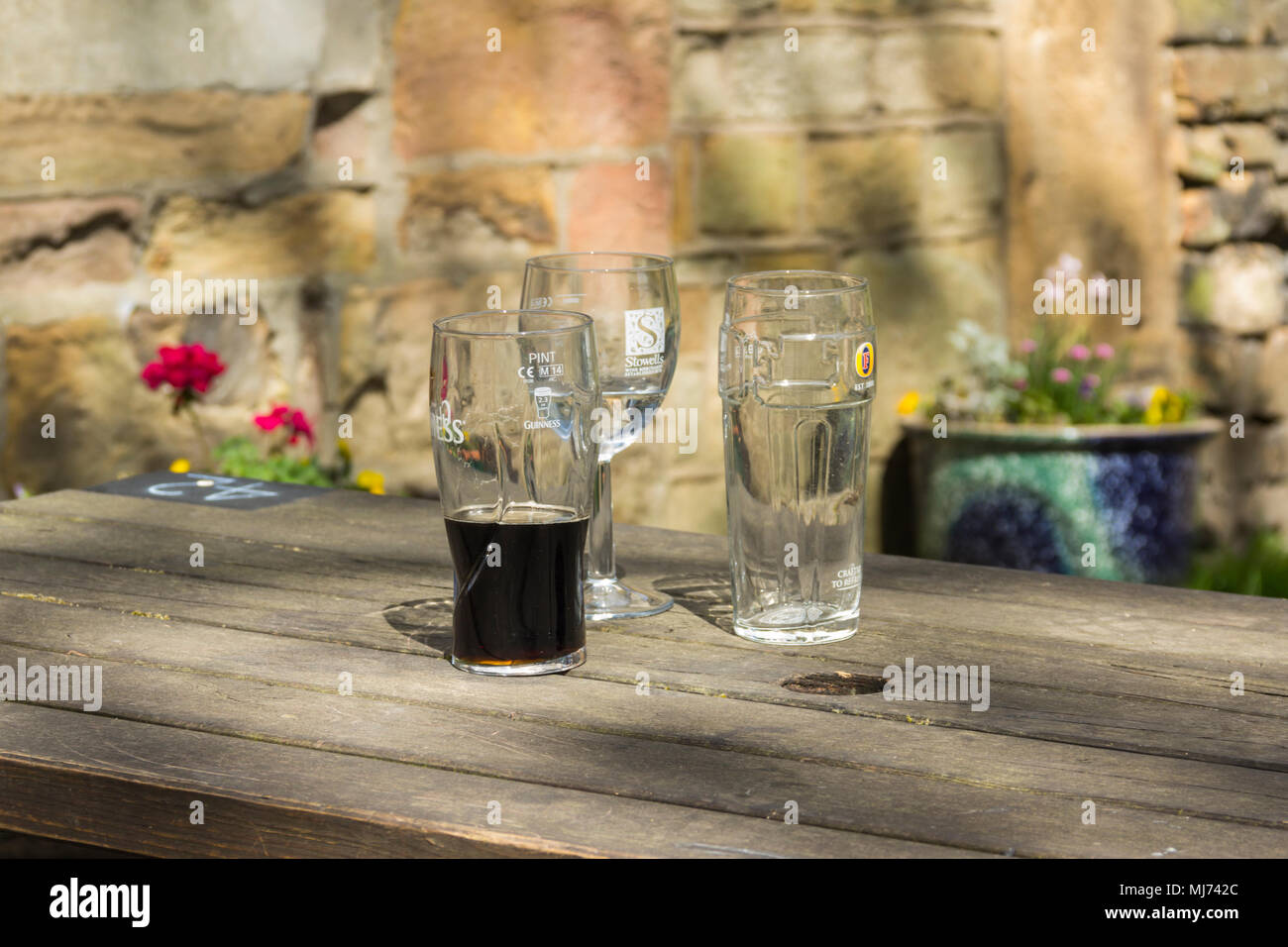Three empty or half empty beer and wine glasses on a outside wooden pub table in a beer garden. The glasses are branded Guinness, Stowells and Fosters Stock Photo