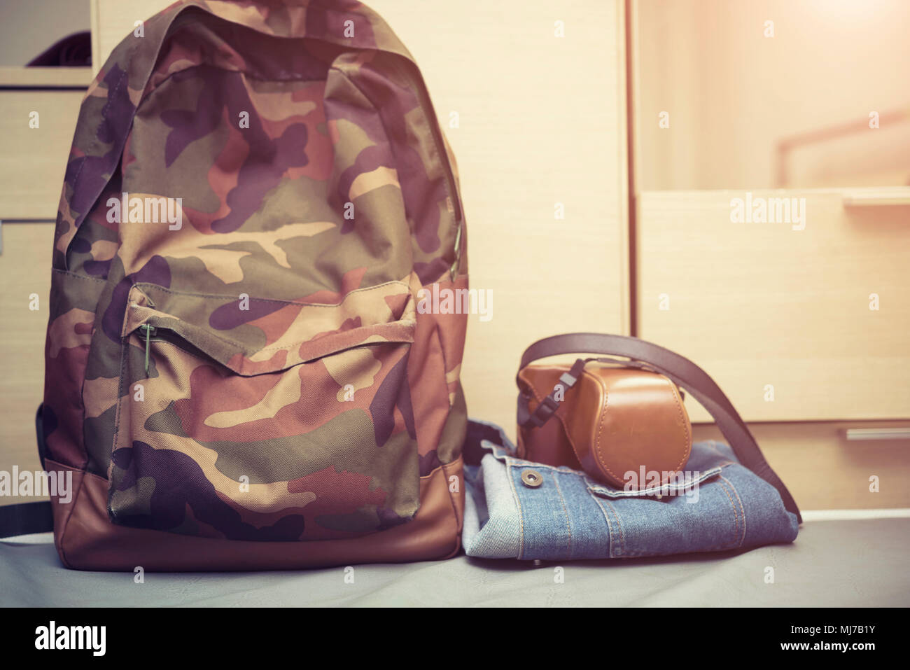 Travel background concept, hipster bag with retro camera case on jeans jacket on bed with free copy space. Stock Photo