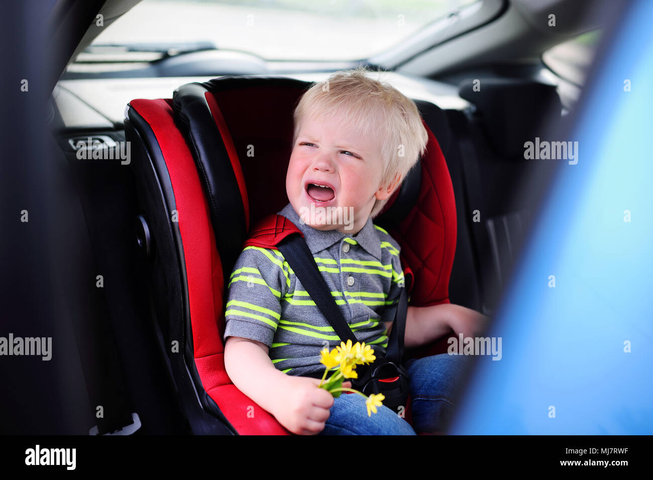 baby boy blondes crying in a children's car seat Stock Photo