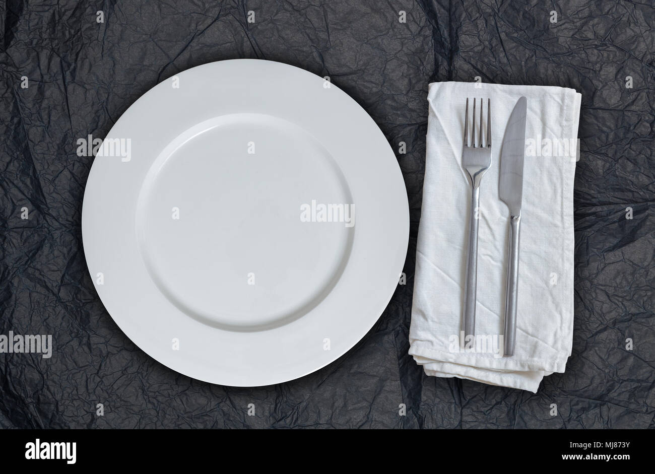 Empty plate and cutlery on black tissue paper. Stock Photo