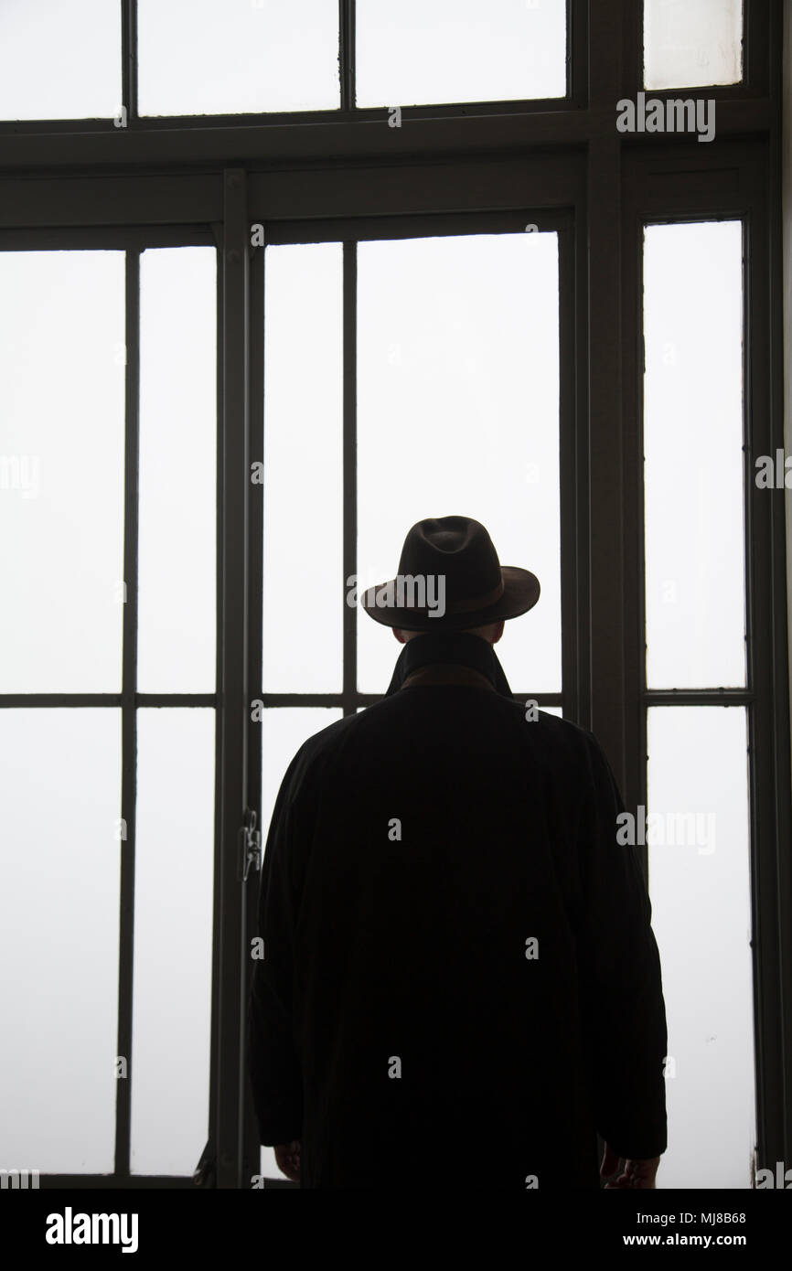 Silhouette of man wearing hat looking out of window. Stock Photo