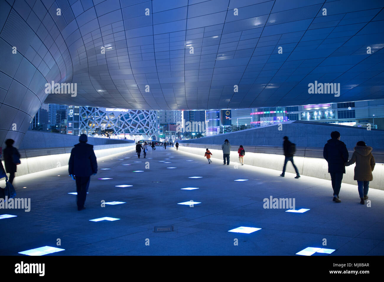Rear View Of People Walking Along Illuminated Walkway Underneath