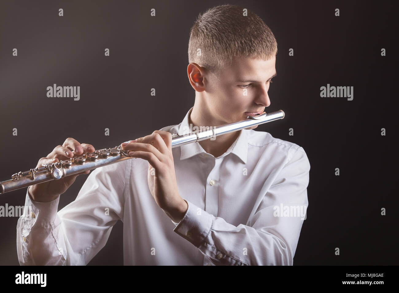 Young man playing the flute on black background Stock Photo