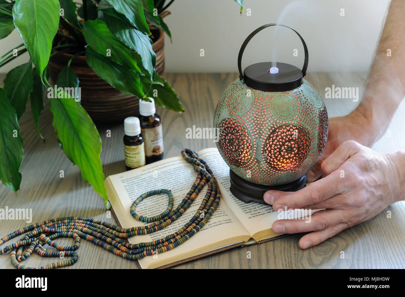 The ultrasonic aroma diffuser is made in the form of an old lamp. Aromatic diffuser is on the wooden table. The man is turning it on. There are essent Stock Photo