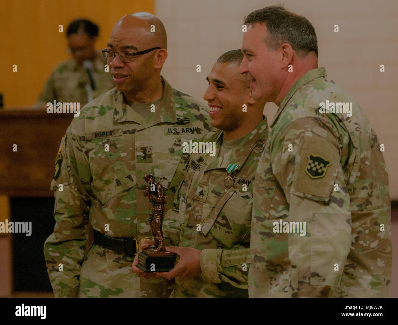 Sergeant Aaron Chavers (center), attached to the 198th Army Band, 99th Readiness Division, stands next to Maj. Gen. A. C. Roper, Commanding General of the 76th Operational Response Command (left) and Command Sgt. Maj. Arlindo Almeida, senior noncommissioned officer of the 99th Readiness Division (right), at Devens Reserve Forces Training Area in Massachusetts, April 19, 2018. Chavers earns the title best warrior, for his command, in the Major Command-level Best Warrior Competition. (U.S. Army Reserve photo by Pvt. Hunter E. Eastman) (Photo cropped and edited for effect.) Stock Photo