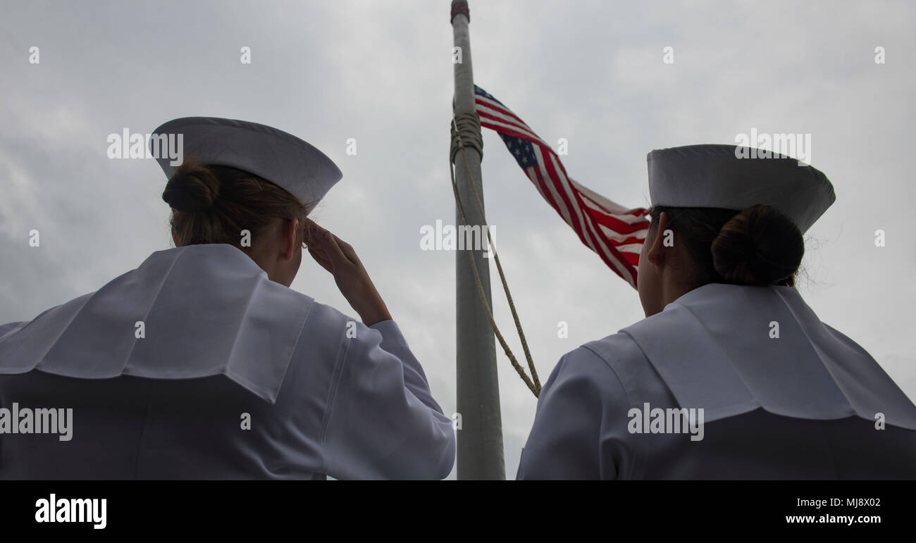 180421-N-BD308-0095 OKINAWA, Japan (April 21, 2018) Sailors lower the national ensign to half-mast to honor former first lady Barbara Bush as the amphibious assault ship USS Wasp (LHD 1) moors in Okinawa to disembark the 31st Marine Expeditionary Unit. Wasp, part of the Wasp Expeditionary Strike Group, has been operating with the MEU for nearly two months as part of a routine patrol in the Indo-Pacific. (U.S. Navy photo by Mass Communication Specialist 3rd Class Levingston Lewis/Released) Stock Photo