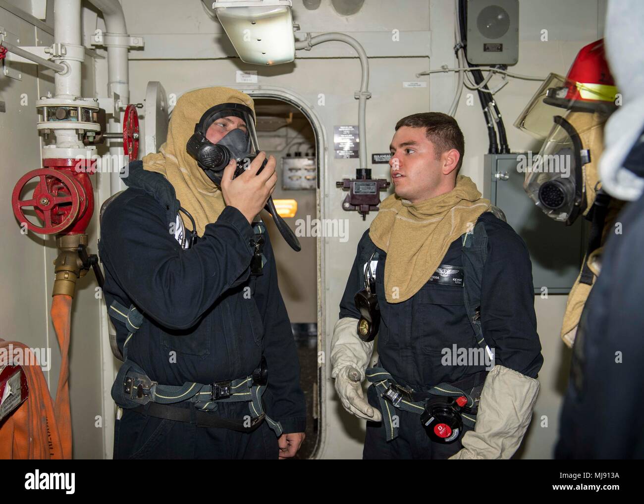 U.S. 5TH FLEET AREA OF OPERATIONS (April 20, 2018) Logistics Specialist 2nd Class Kevin Ortega, right, gives Machinist’s Mate 3rd Class Joseph Mele self-contained breathing apparatus training during a general quarters drill aboard the Wasp-class amphibious assault ship USS Iwo Jima (LHD 7) April 20, 2018. Iwo Jima, homeported in Mayport, Fla., is on a regularly scheduled deployment to the U.S. 5th Fleet area of operations in support of maritime security operations to reassure allies and partners, and preserve the freedom of navigation and the free flow of commerce in the region. (U.S. Navy pho Stock Photo