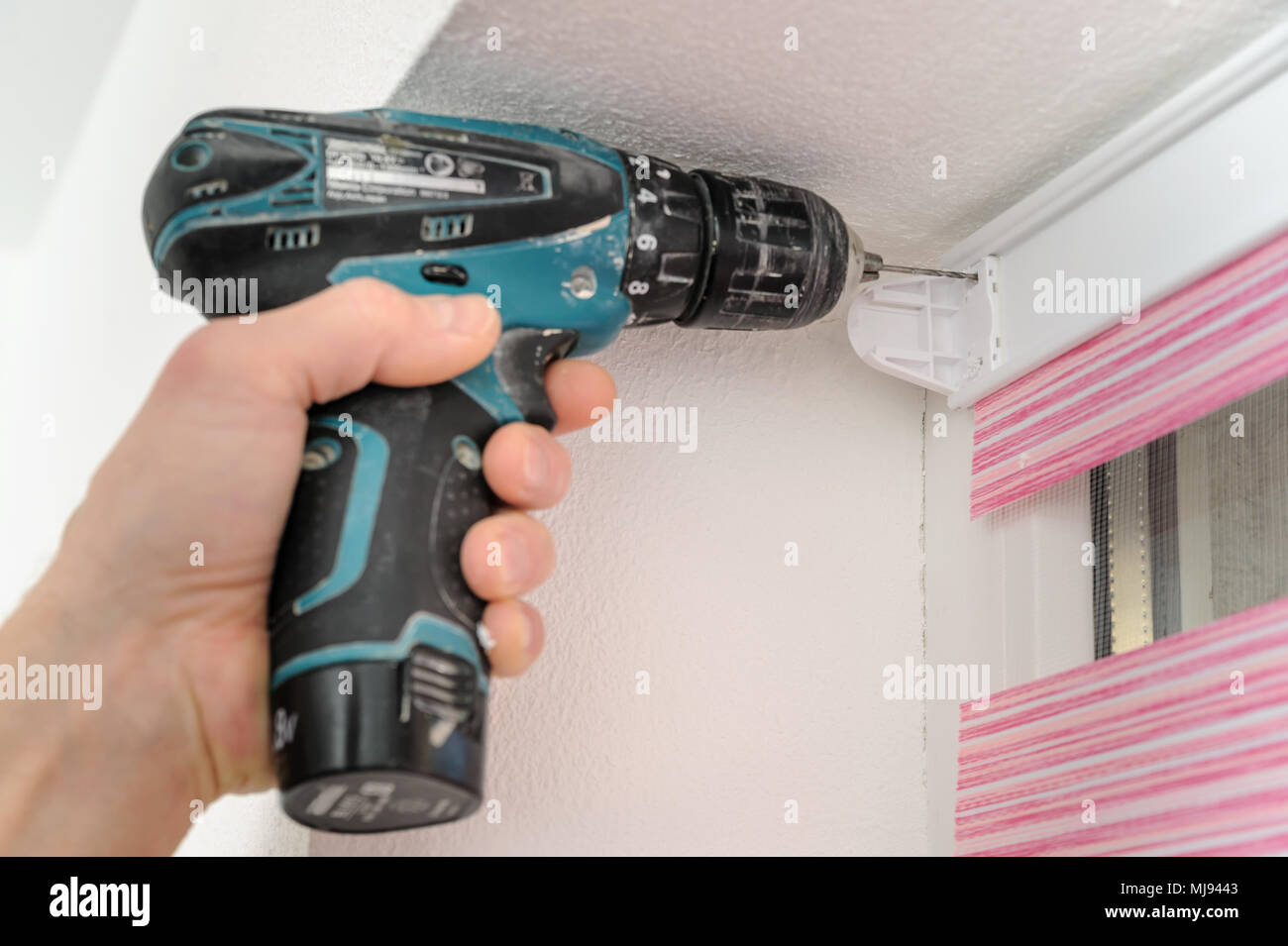 Installing fabric roller blinds. A man drilling holes to fix basis