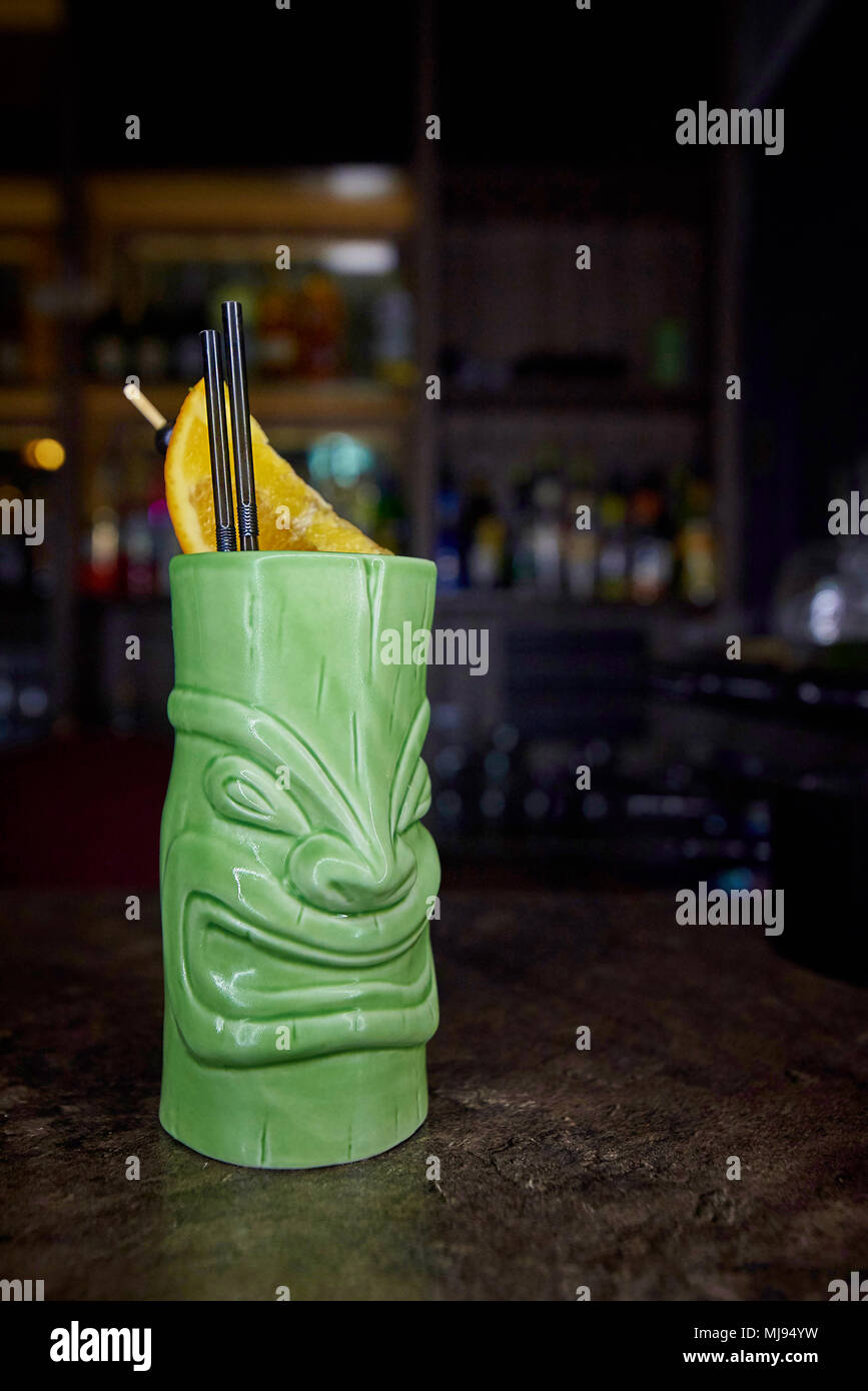 Exotic cocktail in a glass in the form of an ancient deity against the background of a blurred bar. Stock Photo
