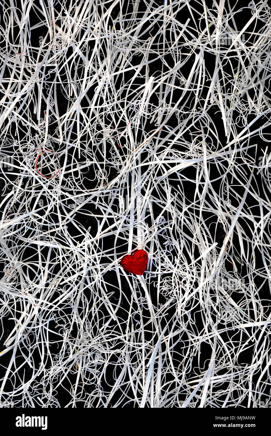 A red glass heart at the centre of a tangle of card offcuts on a background of slate. Stock Photo