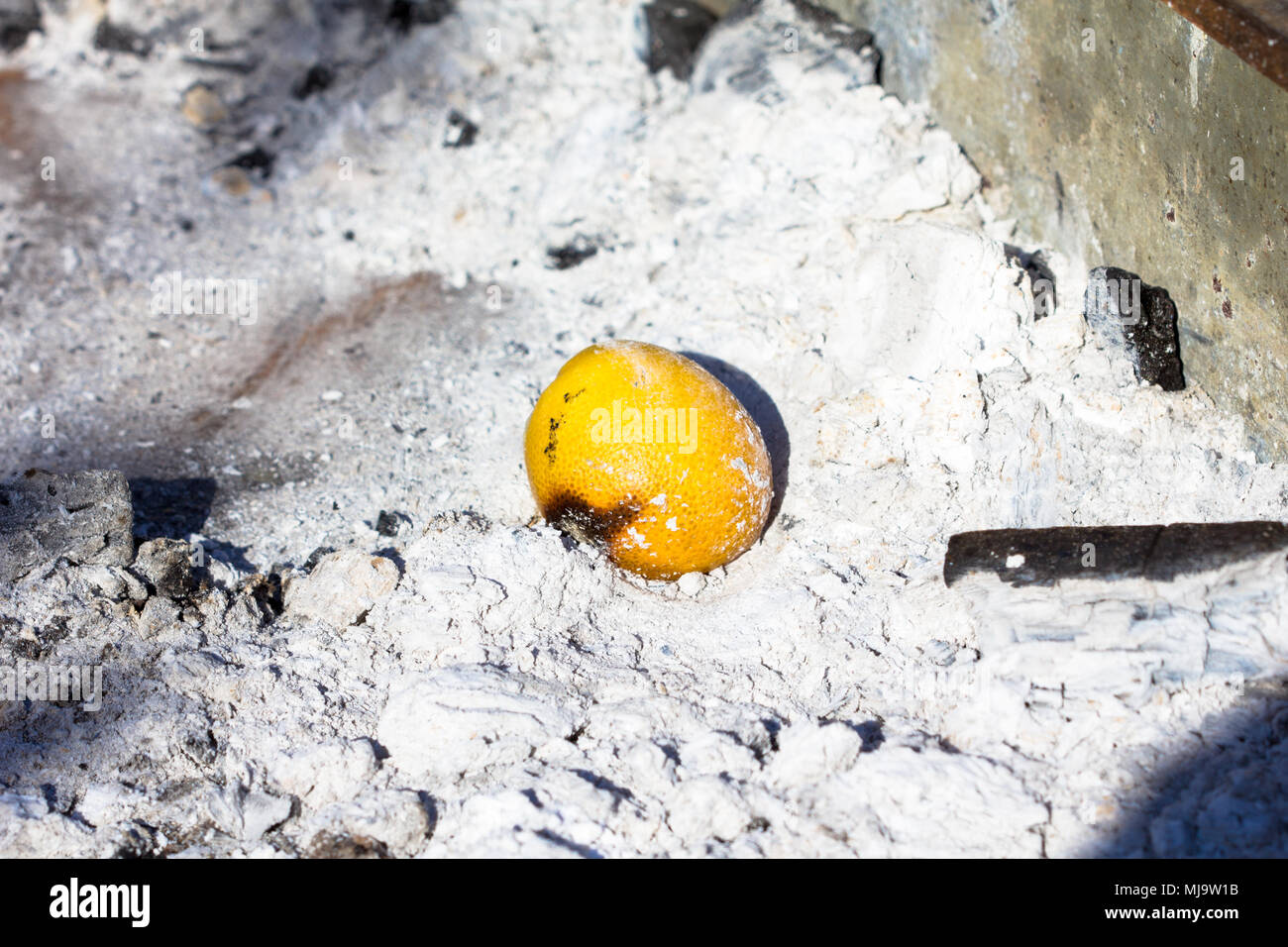 A lemon left burning inside the charcoal tray of a barbecue Stock Photo
