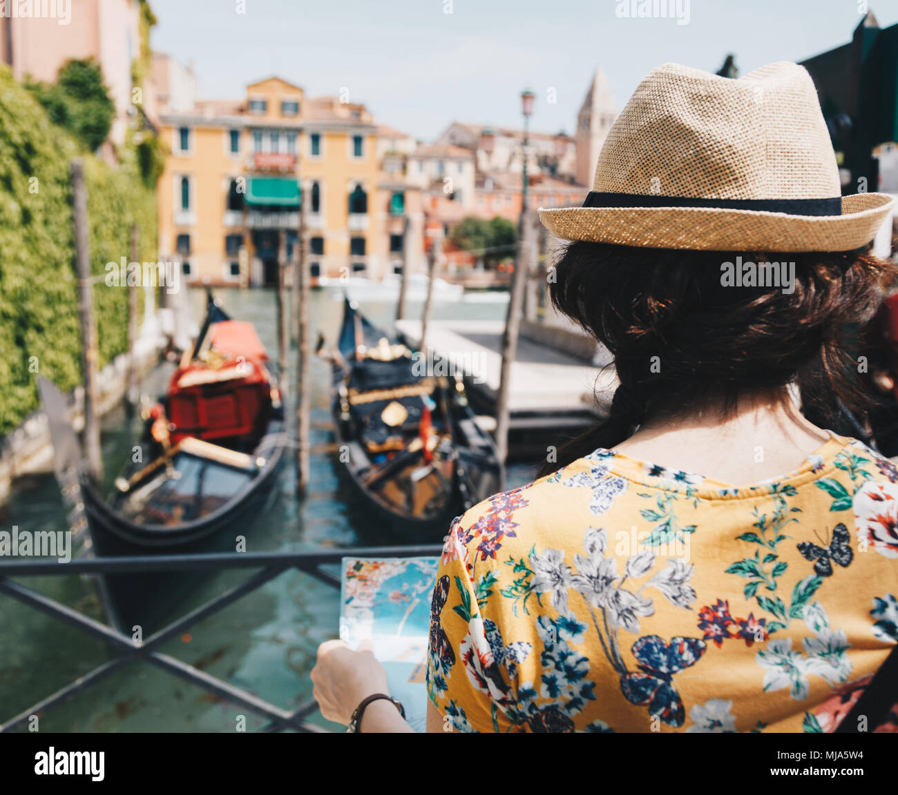 Back view of traveler woman with hat holding paper map with blurred gondola on the background in Venice - Italy. Stock Photo