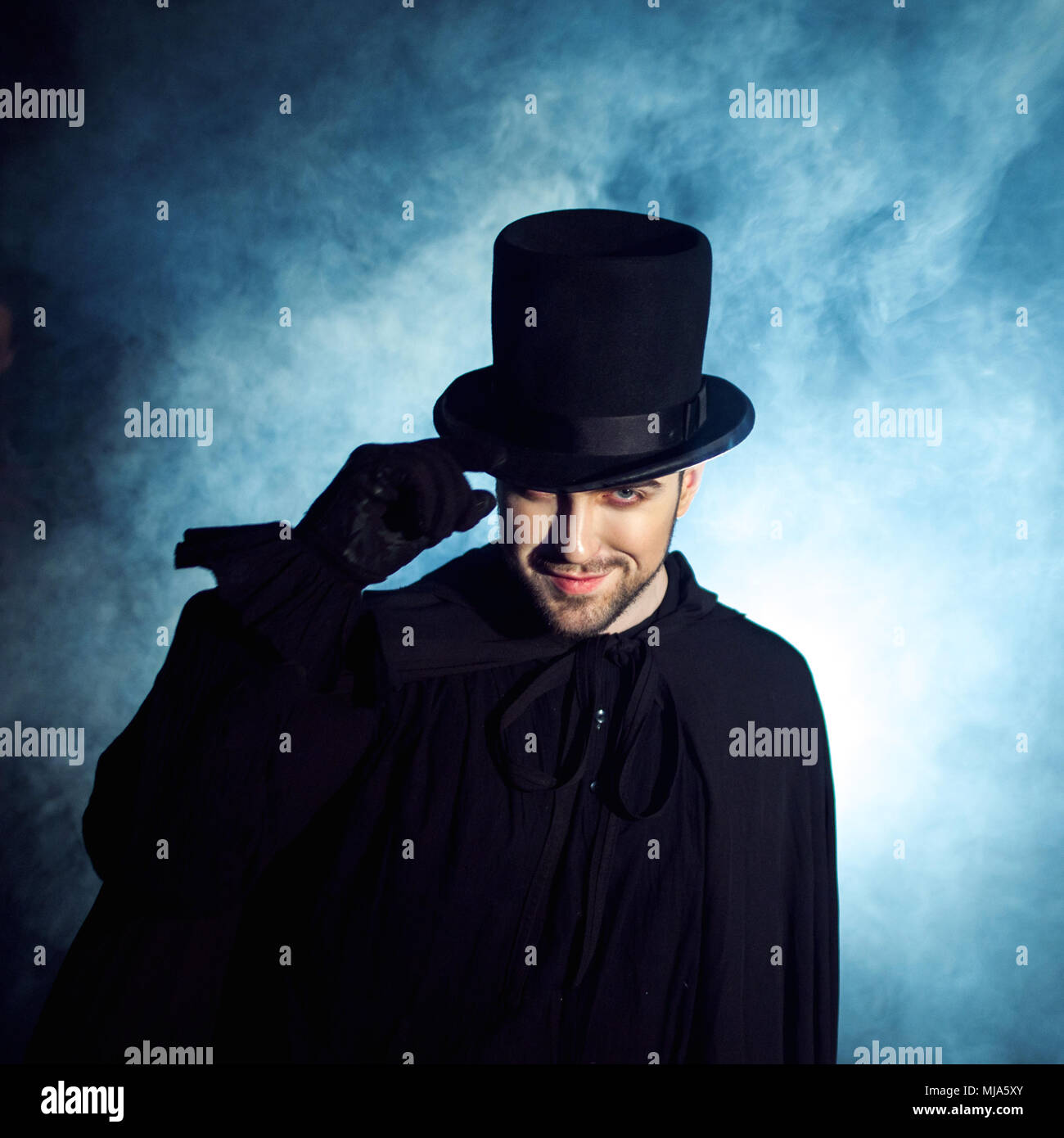 Man in a black top hat and cloak. Demonic image. Magician illusionist. Smoke background Stock Photo