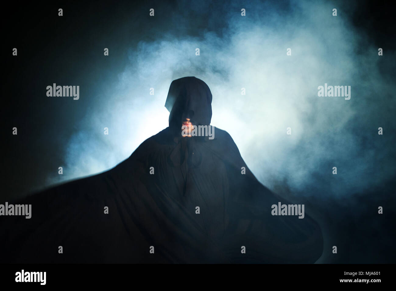 Gloomy image. Man in a black cloak. Demonic image. Magician illusionist. Smoke background Stock Photo
