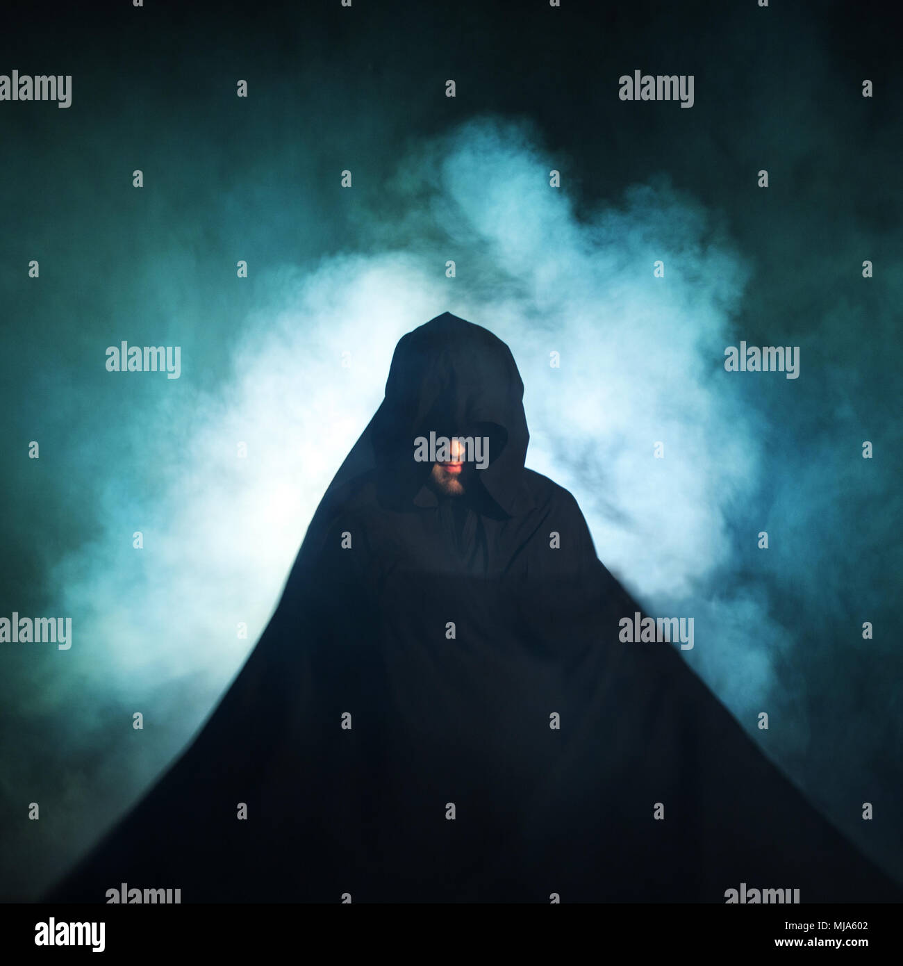Gloomy image. Man in a black cloak. Demonic image. Magician illusionist. Smoke background Stock Photo