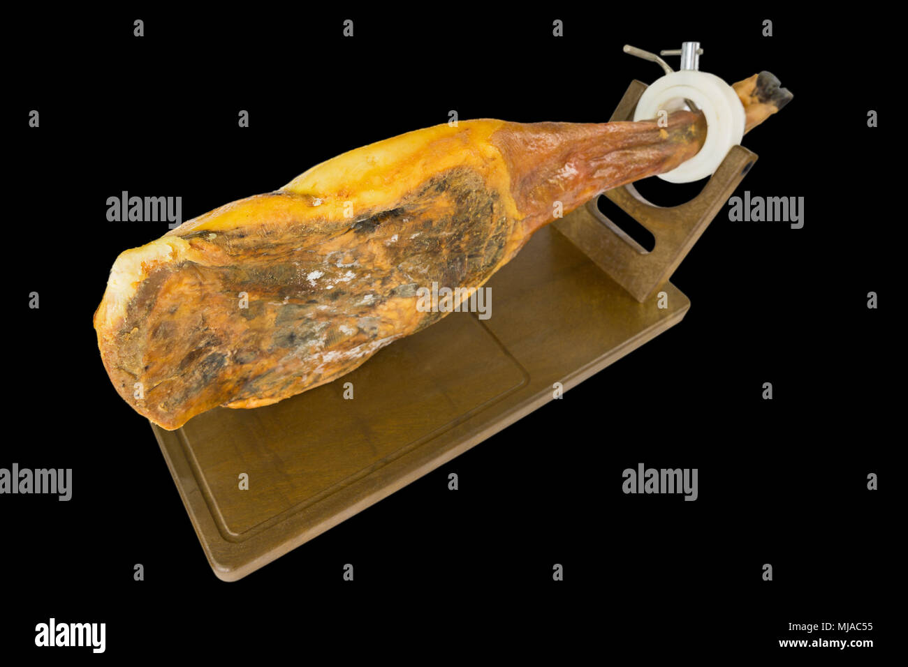 Edge view of whole serrano ham leg over wood, black background Stock