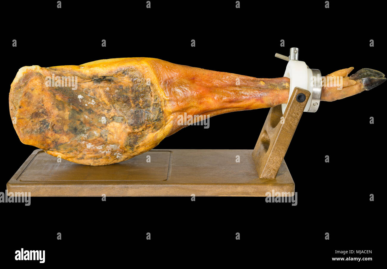 Edge view of whole serrano ham leg over wood, black background Stock
