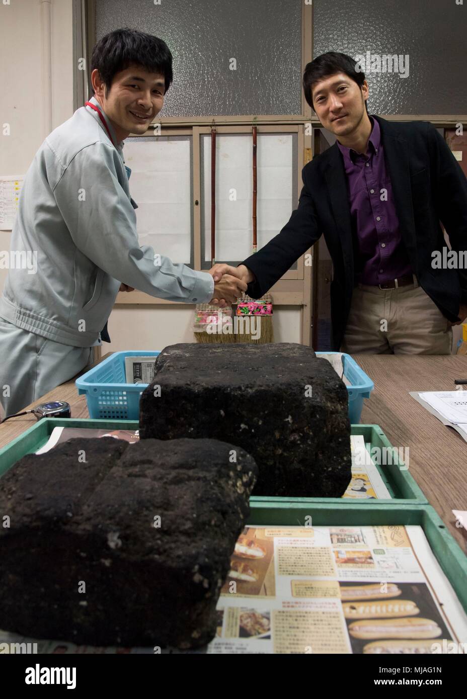 SASEBO, Japan (Apr. 25, 2018) Sasebo City archeologist Atsushi Kawachino and Commander, Fleet Activities Sasebo Cultural Resources Manager Sean Suk shake hands after the turnover of three early 20th century Imperial Japanese Navy coal briquettes to Sasebo City Apr. 25, 2018.  The rare briquettes were fuel for naval vessels and were manufactured by the Tokuyama naval fuel depot in Yamaguchi Prefecture. These were dredged up in CFAS waters during an environmental resources survey conducted in February and turned over to Sasebo City for curation and display. (U.S. Navy photo by Mass Communication Stock Photo