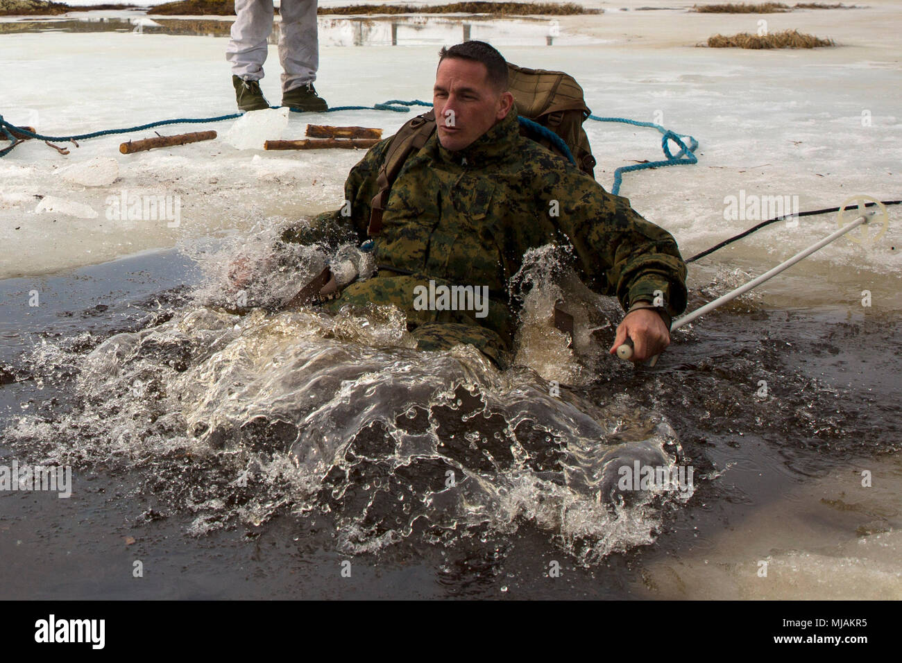 Black Sea Rotational Force and Marine Rotational Force-Europe 18.1 Sgt. Maj. Paul Schuster jumps into icy waters to be the second individual from his unit to complete the polar plunge during a winter warfare training exercise at Haltdalen Training Center, Norway, April 20, 2018. More than 70 Marines and Sailors spent three weeks in the Norwegian wilderness learning cold weather survival techniques, which were taught by Norwegian Soldiers with Home Guard 12. Marines and Sailors who participated in the polar plunge learned how to properly retain their gear and escape after falling through the ic Stock Photo