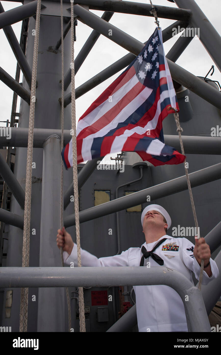 180427-N-WF272-096 PEARL HARBOR, Hawaii (April 27, 2018) Quartermaster 1st Class Matthew Lenerville, from Richardton, N.D., raises the Serapis Flag as the amphibious assault ship USS Bonhomme Richard (LHD 6) arrives at Pearl Harbor, Hawaii for a scheduled port visit. Bonhomme Richard, which had been forward-deployed since 2012 as the Amphibious Force 7th Fleet flagship, is transiting to San Diego as part of a homeport change where it is scheduled to undergo upgrades to operate the F-35B Lightning II. (U.S. Navy photo by Mass Communication Specialist 2nd Class Diana Quinlan/Released) Stock Photo