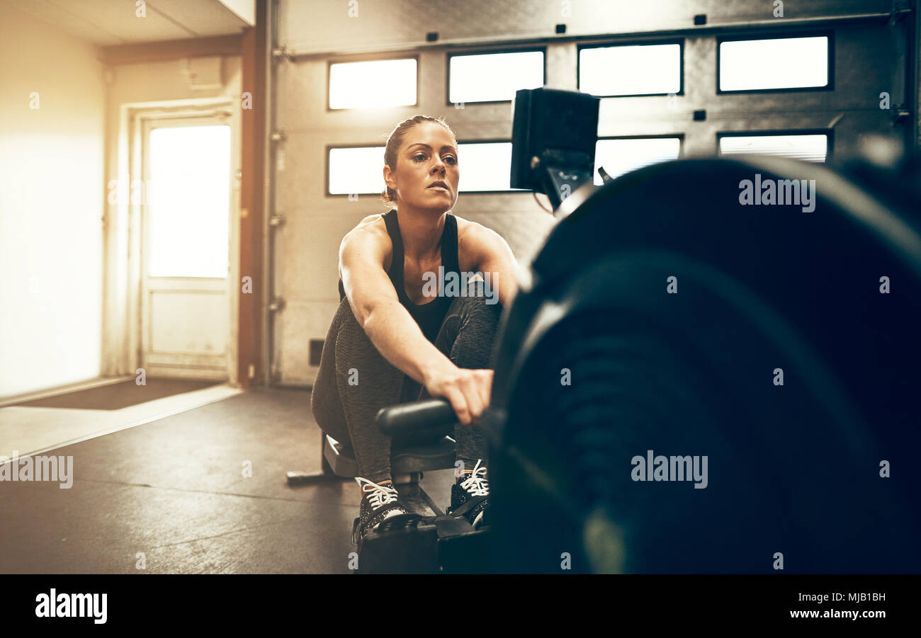 Fit young woman in sportswear exercising on a rowing machine during a ...