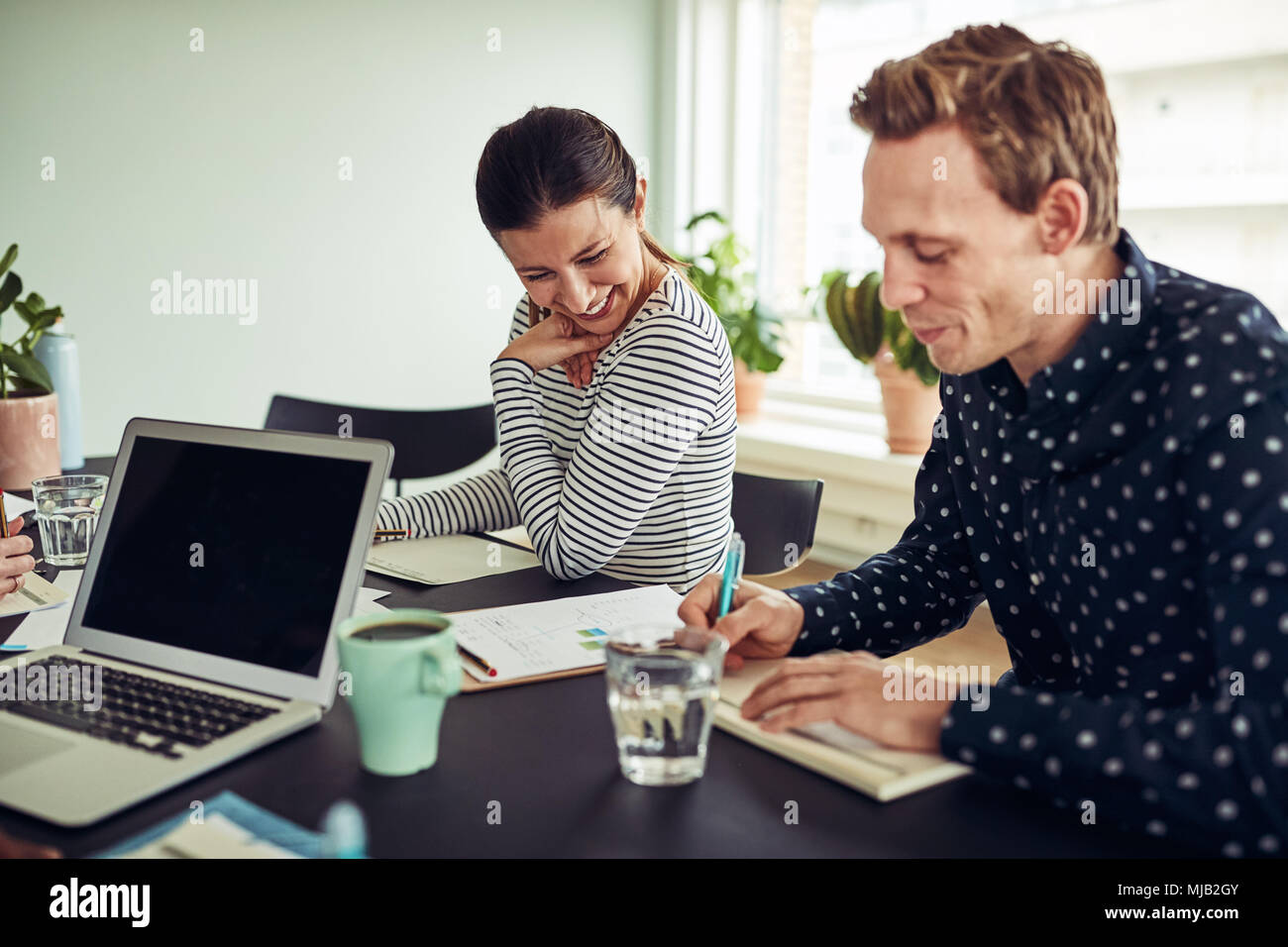 Two smiling young business colleagues sitting together at a table in an office going over paperwork Stock Photo