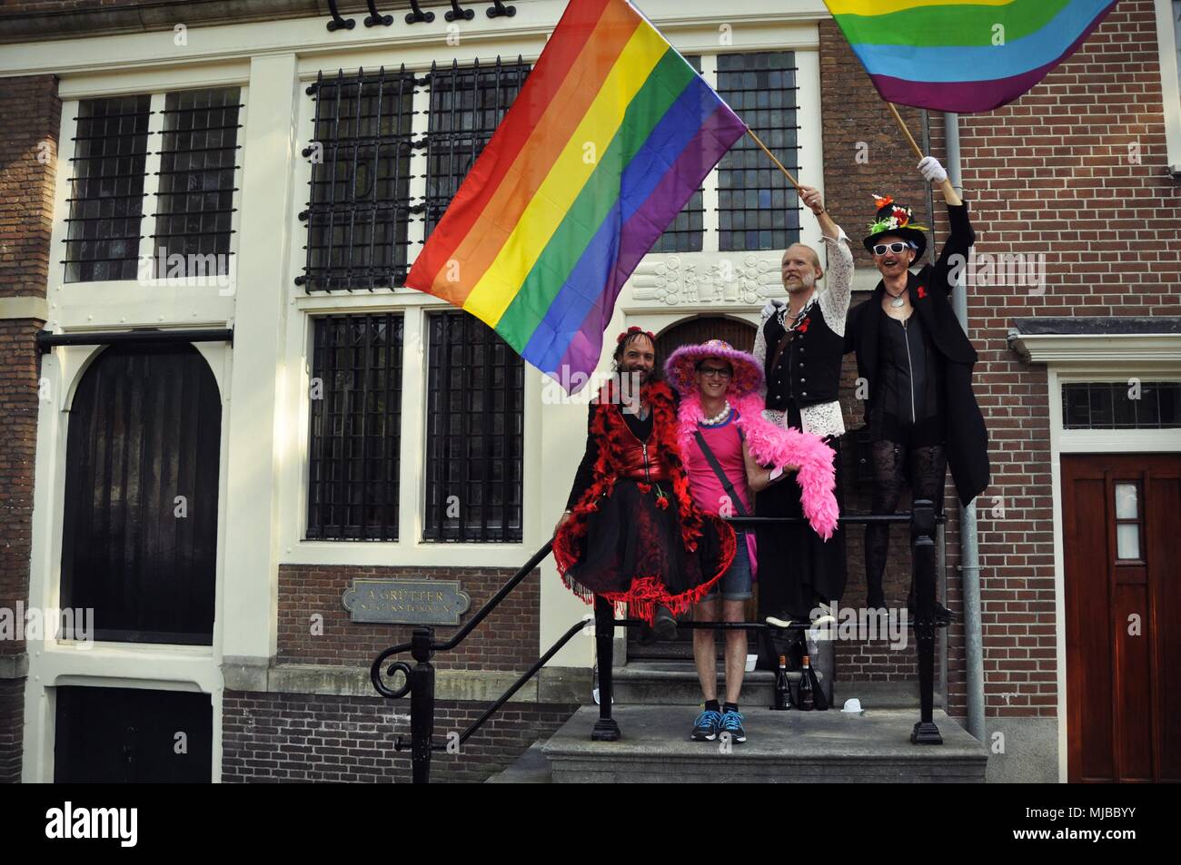 Amsterdam, Netherlands:  Four people in costumes standing on a balcony, waiving rainbow flags at the traditional Amsterdam gay pride event. Stock Photo