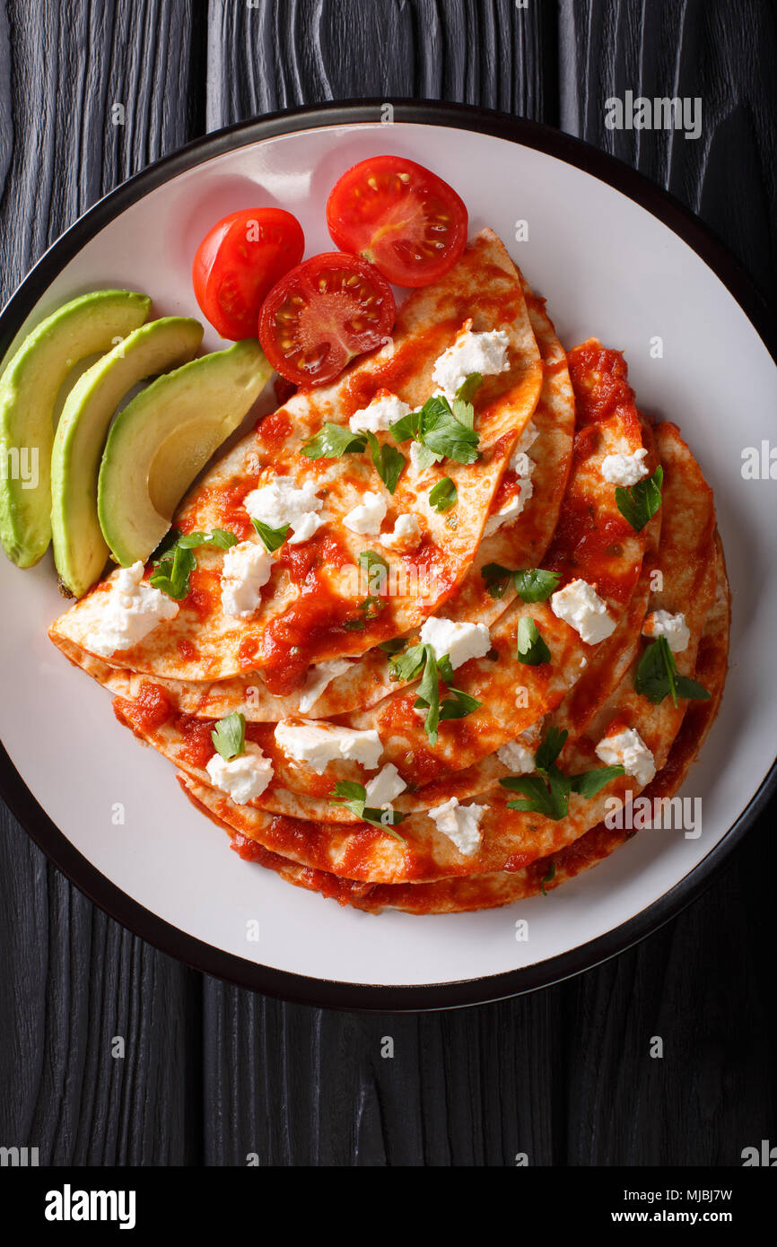 entomatadas with farm cheese and tomato sauce closeup on a plate on a table. Vertical top view