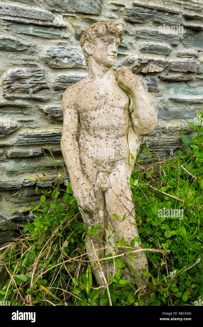 garden ornaments looking like greek statues being slowly overgrown by ivy and clematis growing in the spring sunshine. Stock Photo