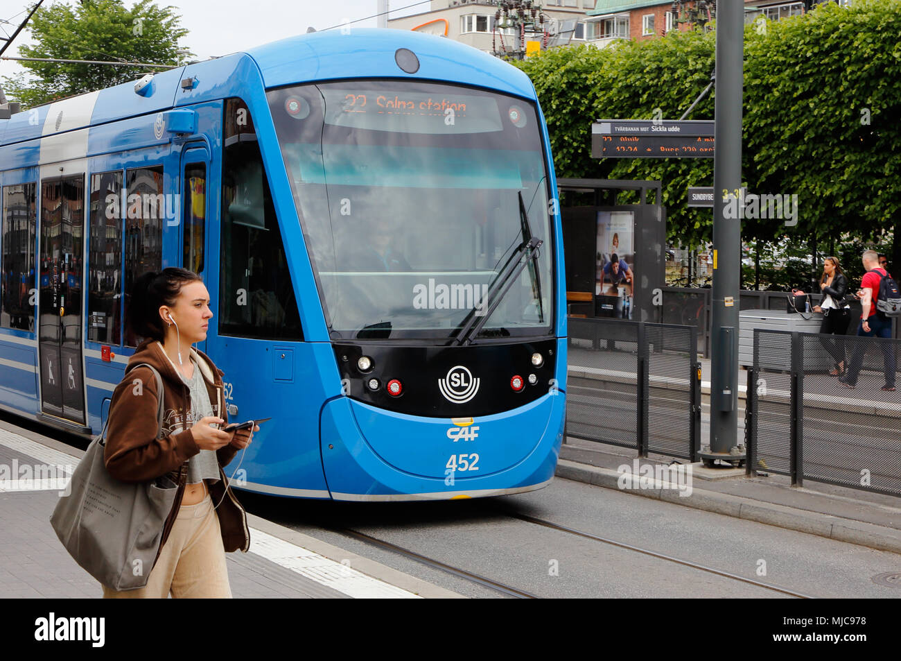 Sundbyberg, Sweden - June 21, 2016: Tram on street tracks in Sunbyberg city center with a woman walking at the tram stop. Stock Photo