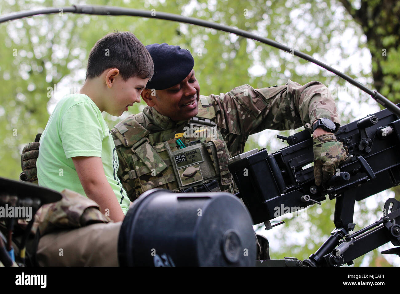U.K. soldier with the 1st The Queen's Dragoon Guards, shows a Polish child a 12.7mm heavy machine gun on top of a Jackal 2A armored vehicle during a bridge opening ceremony in Giżycko, Poland, May 1, 2018. The ceremony was held between the town of Giżycko and the Soldiers of Battle Group Poland: a unique, multinational coalition of U.S., U.K., Croatian and Romanian soldiers who serve with the Polish 15th Mechanized Brigade as a deterrence force in support of NATO’s Enhanced Forward Presence. (U.S. Army photo by Spc. Hubert D. Delany III /22nd Mobile Public Affairs Detachment)    Stock Photo