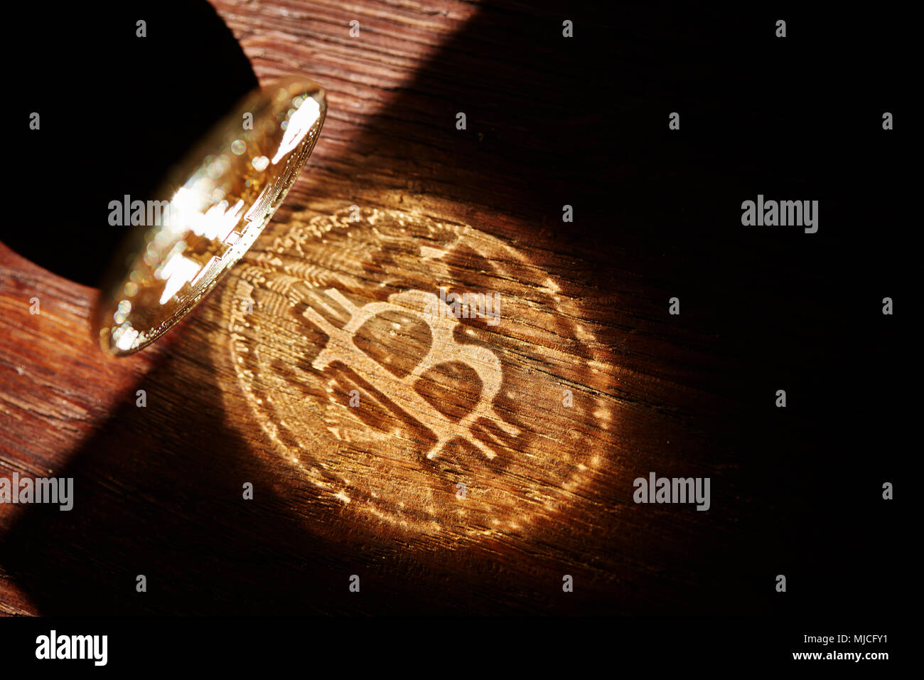 Bitcoin cryptocurrency with its shadow on wooden table, close-up, macro, selective focus, shallow depth of field. Some copy space for your inscription Stock Photo