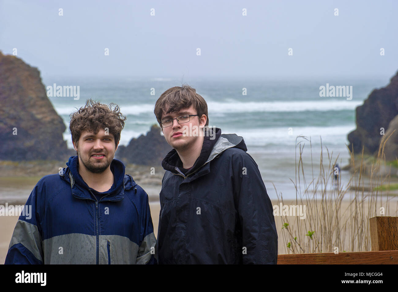Two brothers pose, in the rain, for camera before heading out on  Arcadia beach seen in the background on the Oregon Coast Stock Photo