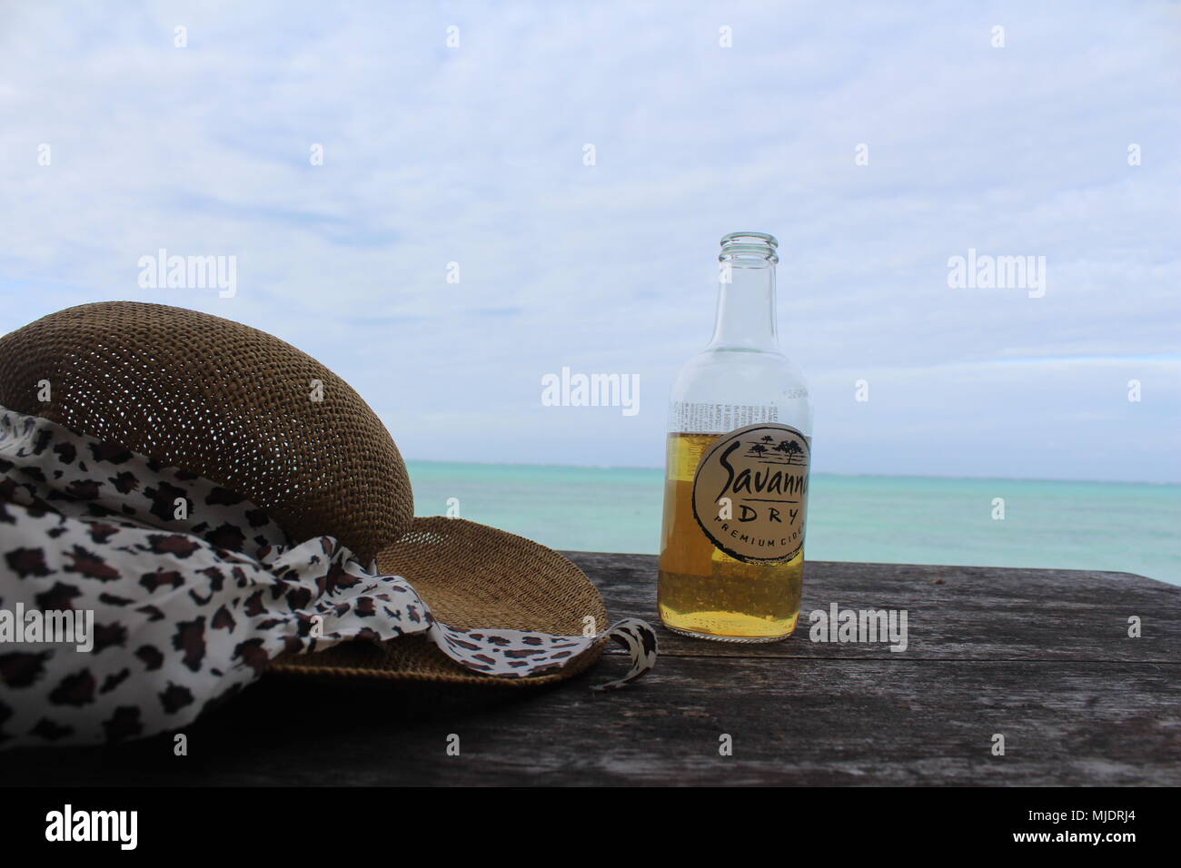Savannah Dry apple cider and a beach hat on a table with clear blue water sea in the background. Zanzibar, Tanzania Stock Photo