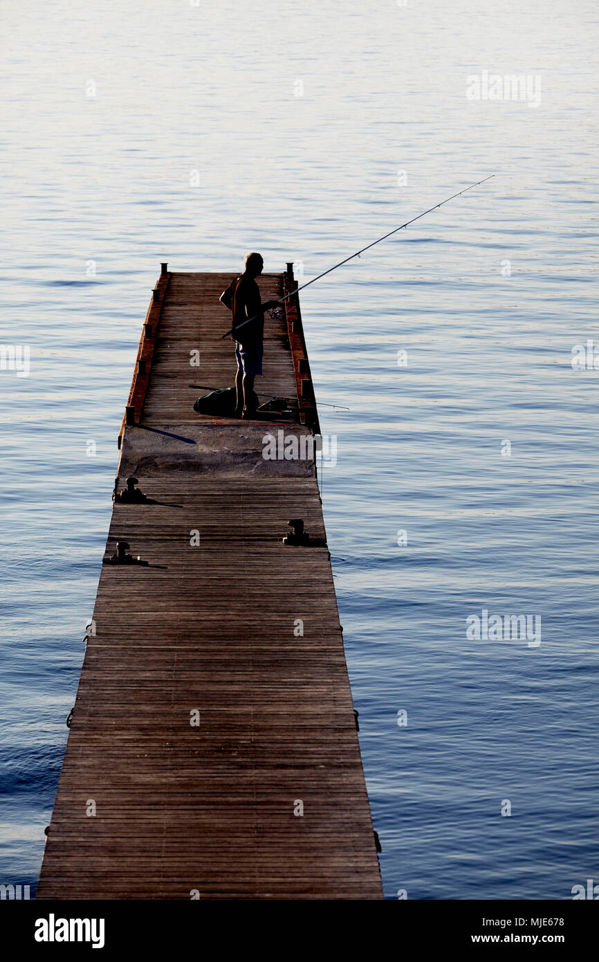 Angler on a wooden landing stage by the sea Stock Photo
