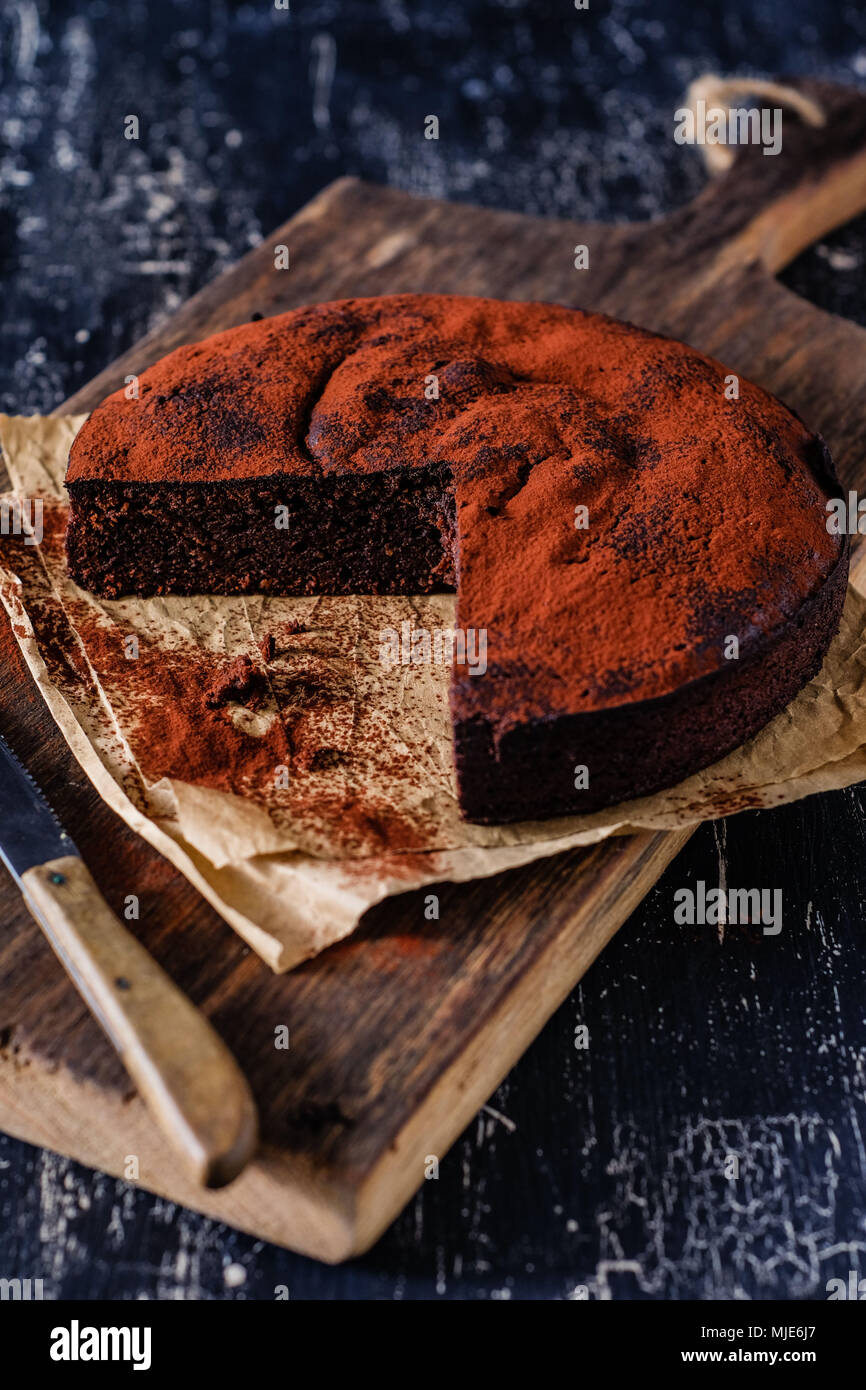 Dark chocolate cake on an old wooden board, parts of it already cut off Stock Photo