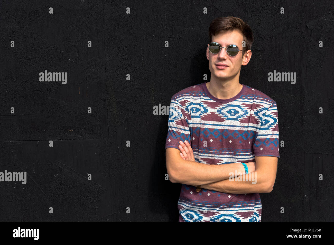 young man with sunglasses in front of black wall, arms crossed, half portrait, Stock Photo