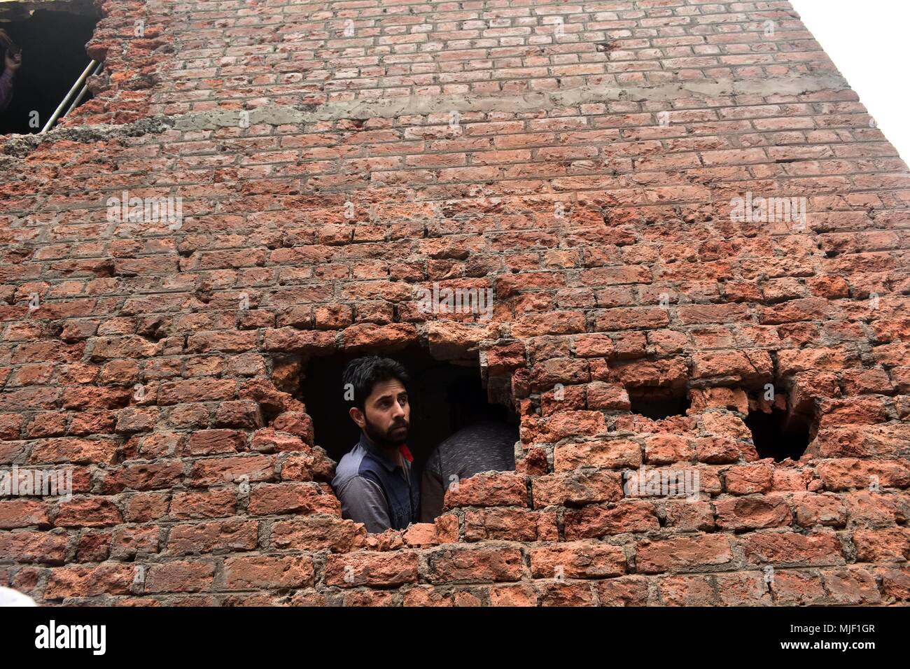 Kashmir, India, 5 May 2018.  A Kashmiri resident looks out of the damaged hous militants were trapped during an encounter in Srinagar, Indian administered Kashmir. Three suspected militants and one civilian have been killed while three Indian paramilitary men sustained injuries in a gun battle in Srinagar, the summer capital of Indian administered Kashmir. The encounter started after government forces cordoned off a Chattabal area following the presence of militants in the area, officials said.  the militants were believed Credit: ZUMA Press, Inc./Alamy Live News Stock Photo