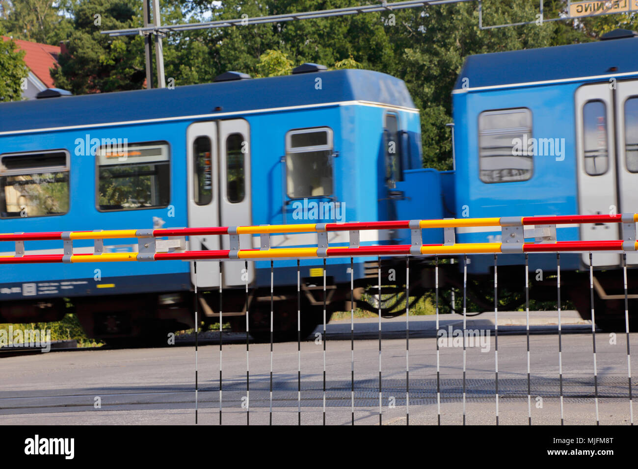 Level crossing with closed barriers and a passing blue train. Stock Photo