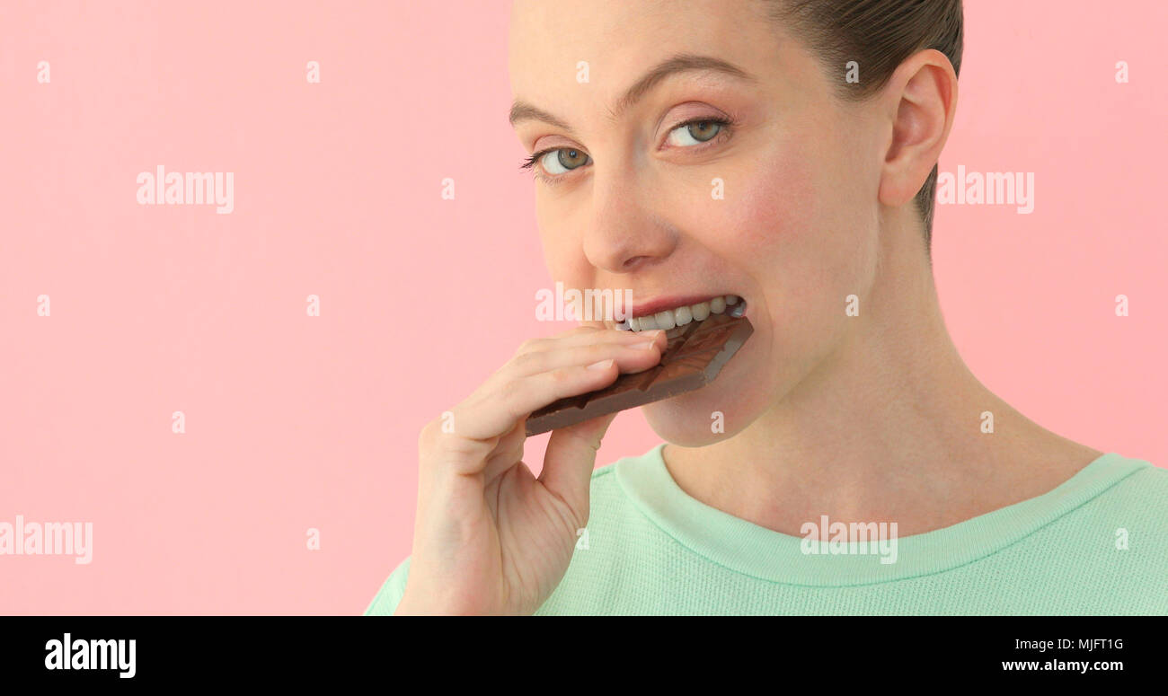 Woman eating chocolate over pink background Stock Photo
